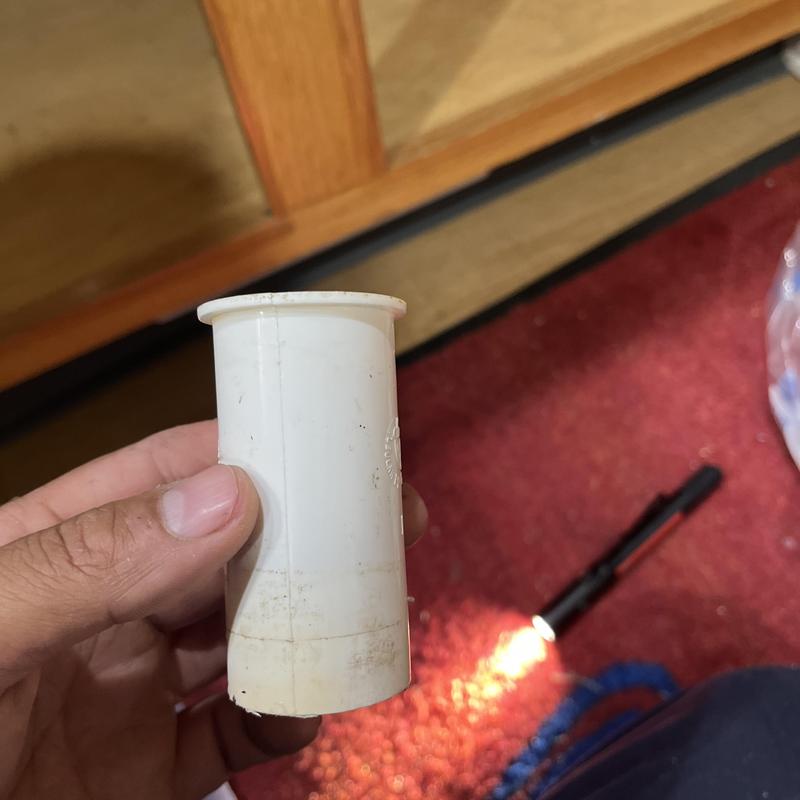Kitchen sink PVC pipe section held in hand with flashlight on floor