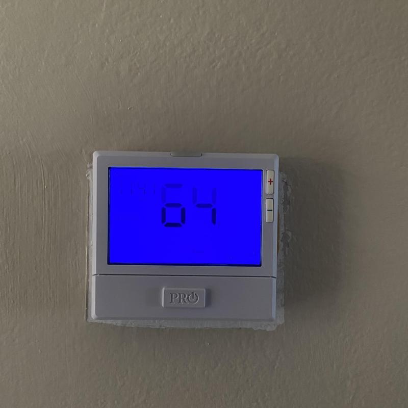 Heat pump thermostat display showing temperature set at 64°F