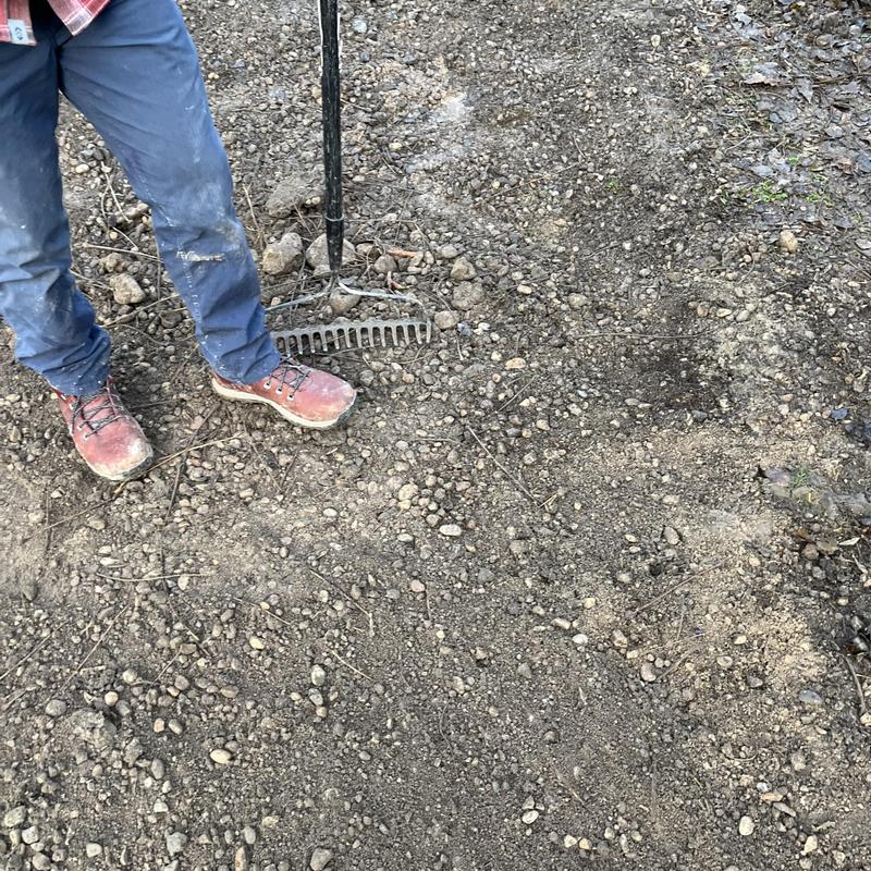 Concrete pipe excavation site with rake and worker boots