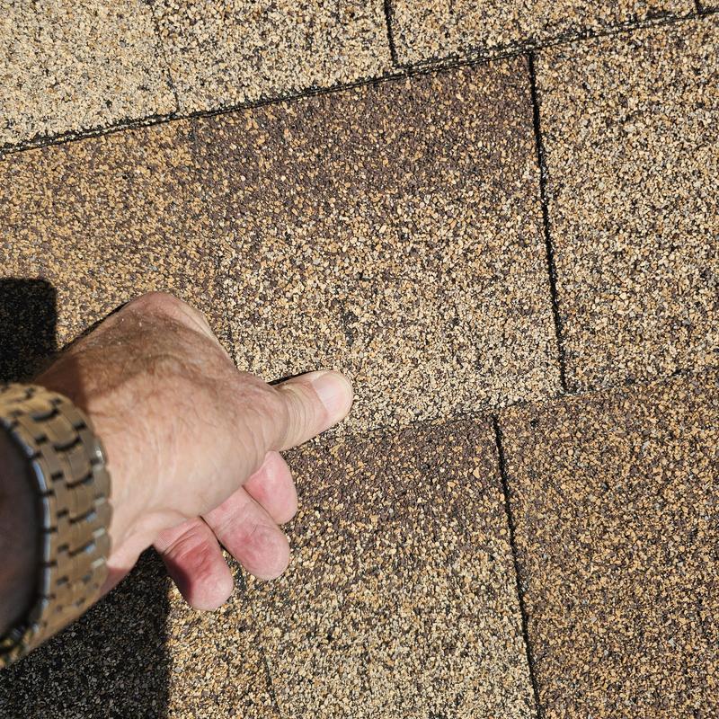 Asphalt shingles hail damage close-up with hand pointing