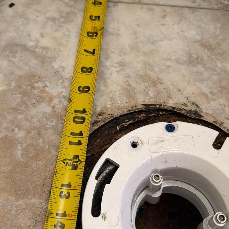 Toilet flange with measuring tape on tile floor