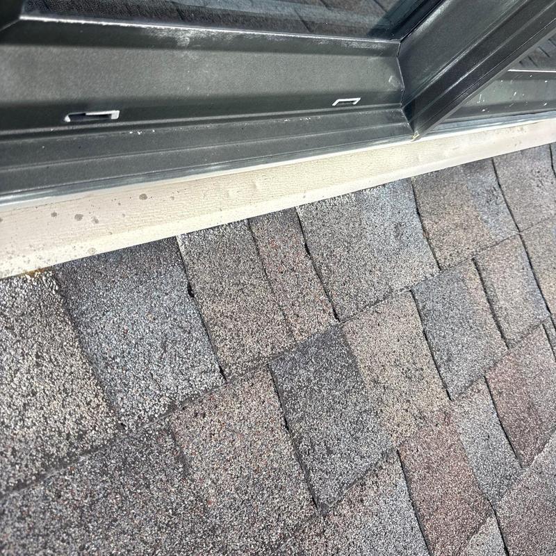 Asphalt roof shingles showing hail damage near window flashing