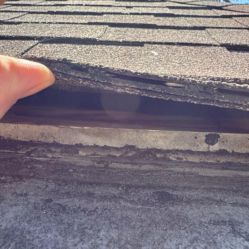 Roof shingles lifted showing damage and wear beneath