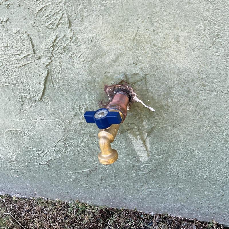 Quarter turn hose bib with blue handle on exterior wall