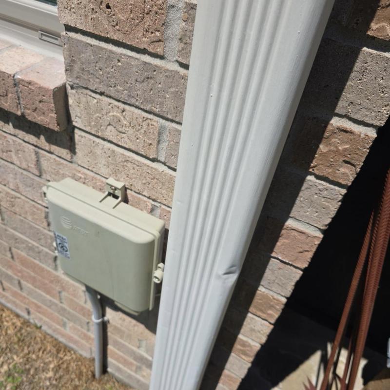 Downspout with dent damage near brick wall and utility box