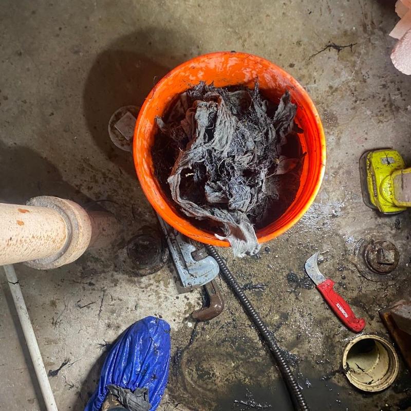 Drain pipe clog removal debris in orange bucket