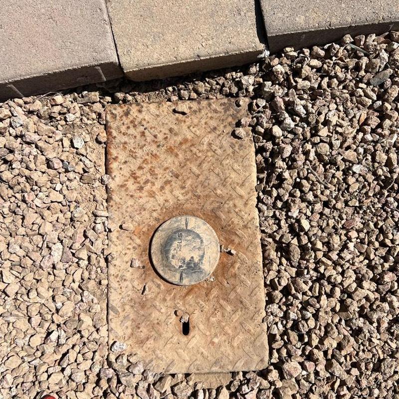 Water meter cover surrounded by gravel and pavers outdoors