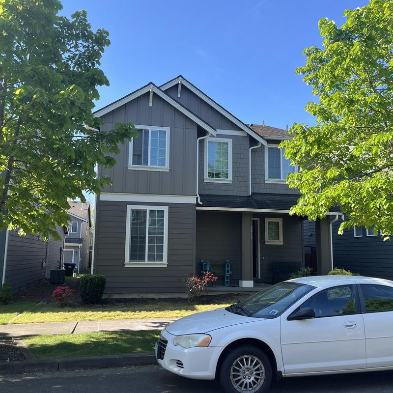 Roof shingles on two-story house with white car parked nearby