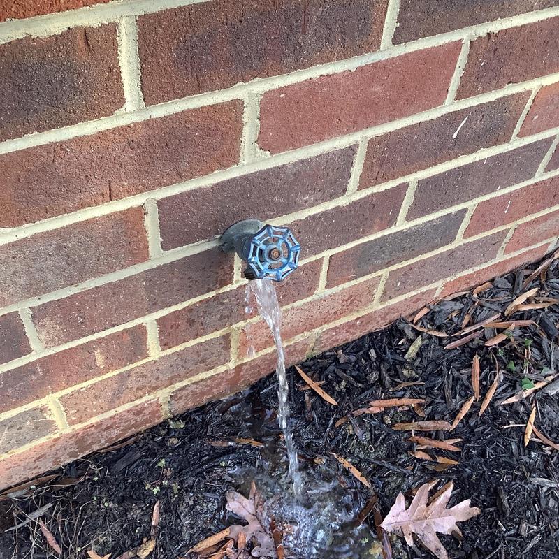 Hose bib water spout with running water on brick wall Hose bib water spout with running water on brick wall