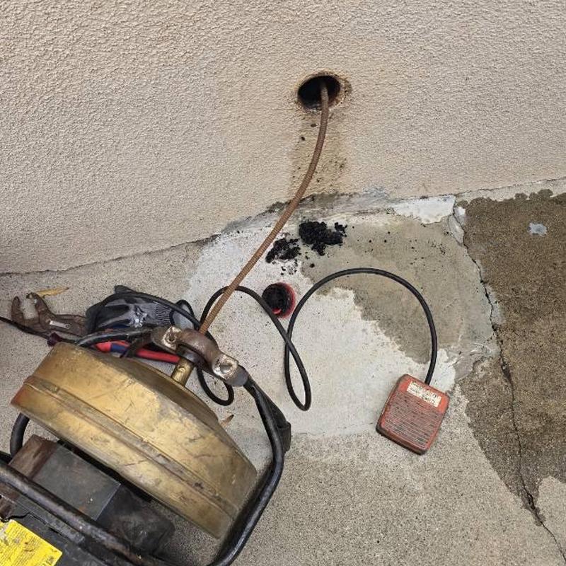 Drain snake clearing kitchen clean-out clog in concrete wall