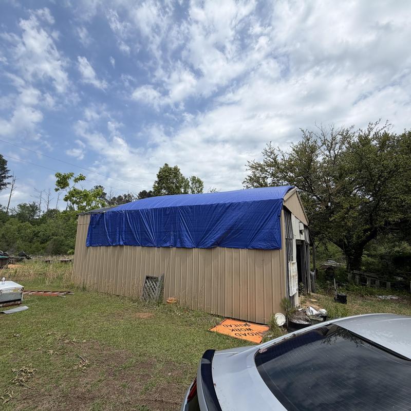 Metal barn roof with blue tarp cover after tree damage