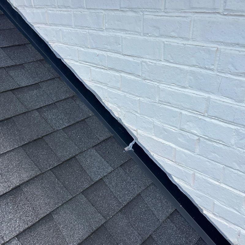 Roof flashing along shingled roof and brick wall junction