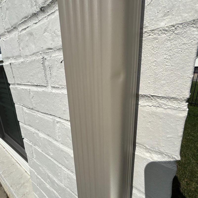 Metal downspout with dent near white brick wall exterior