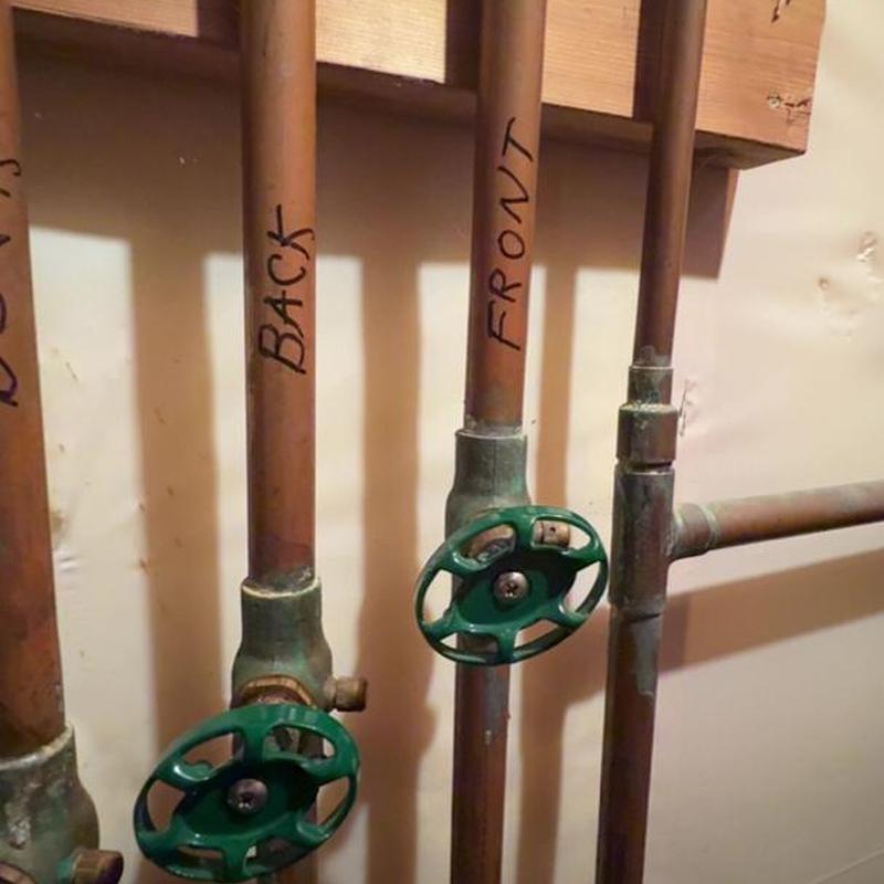 Shutoff valves on labeled copper pipes with green handles