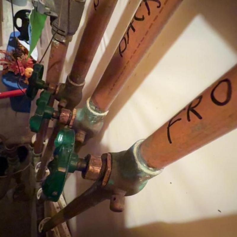 Copper shutoff valves on plumbing pipes with green handles
