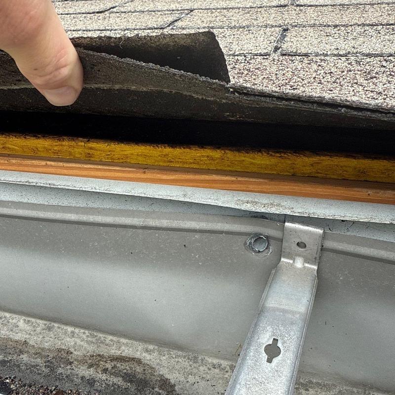 Asphalt shingles lifted showing underlying damage and nail rust