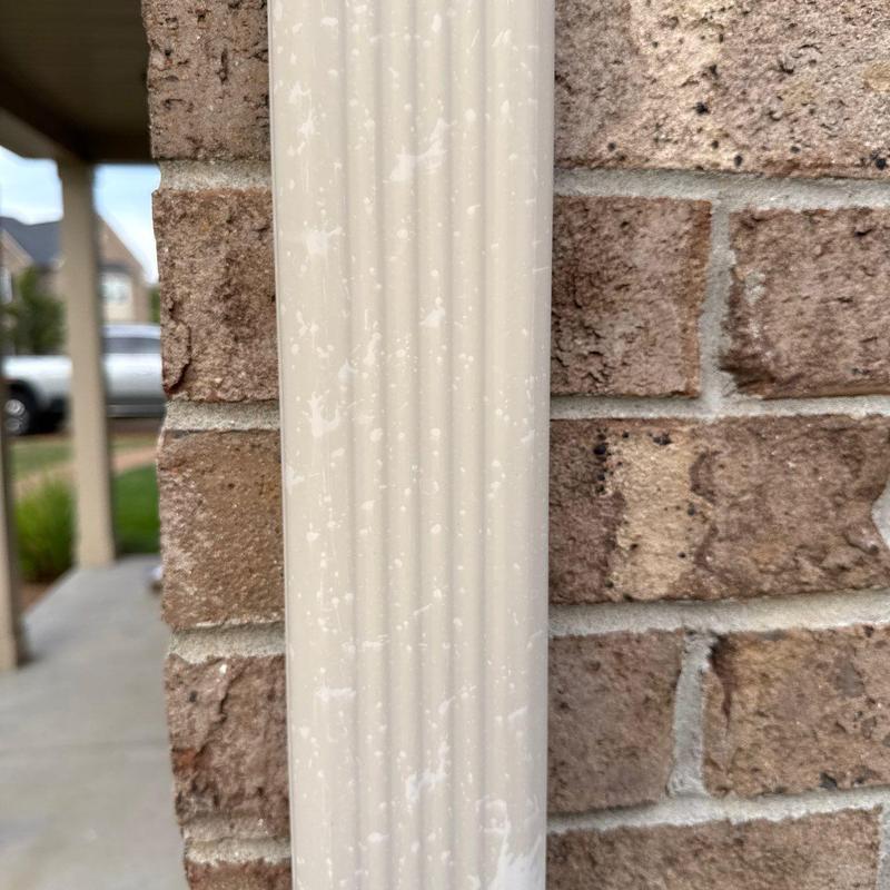 PVC downspout with white paint splatter on brick wall