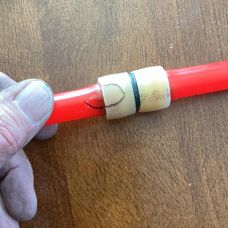 Red plastic water line with damage marking near fitting Red plastic water line with damage marking near fitting