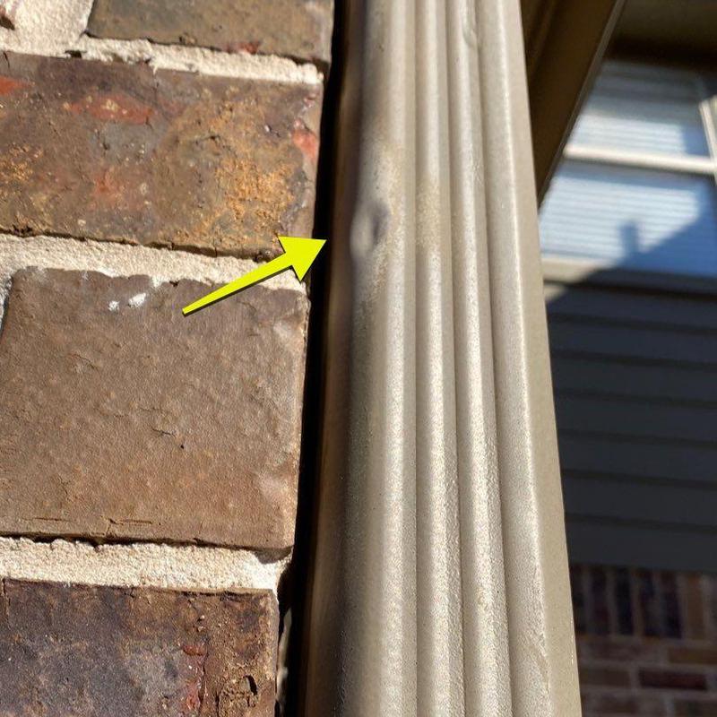 Metal downspout dent damage next to brick wall