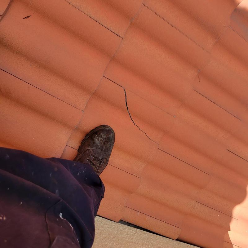 Concrete tile roof with cracked tile and foot visible