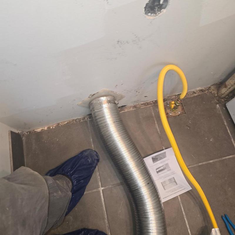 Dryer vent duct and yellow gas whip installed on tile floor