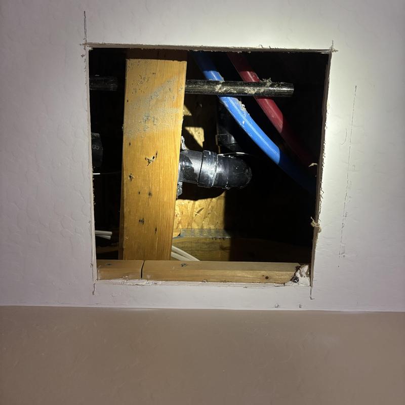 PVC drain pipe with red and blue PEX pipes behind drywall opening PVC drain pipe with red and blue PEX pipes behind drywall opening