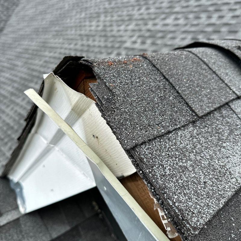 Roof shingles and flashing damaged by hail on ridge edge