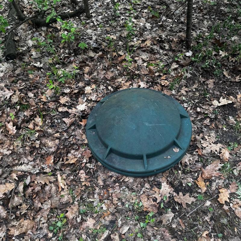 Sump pump pit cover surrounded by leaves outdoors