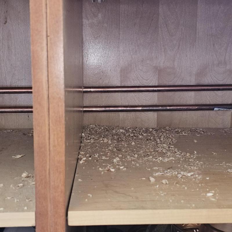 Copper water pipes inside kitchen cabinet with wood shavings