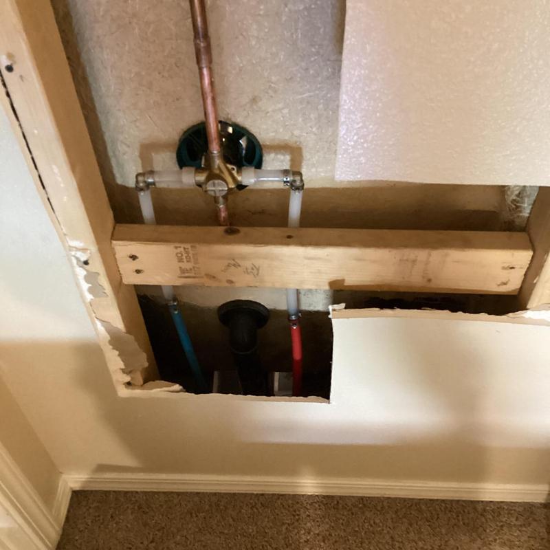 Shower valve plumbing behind opened drywall panel