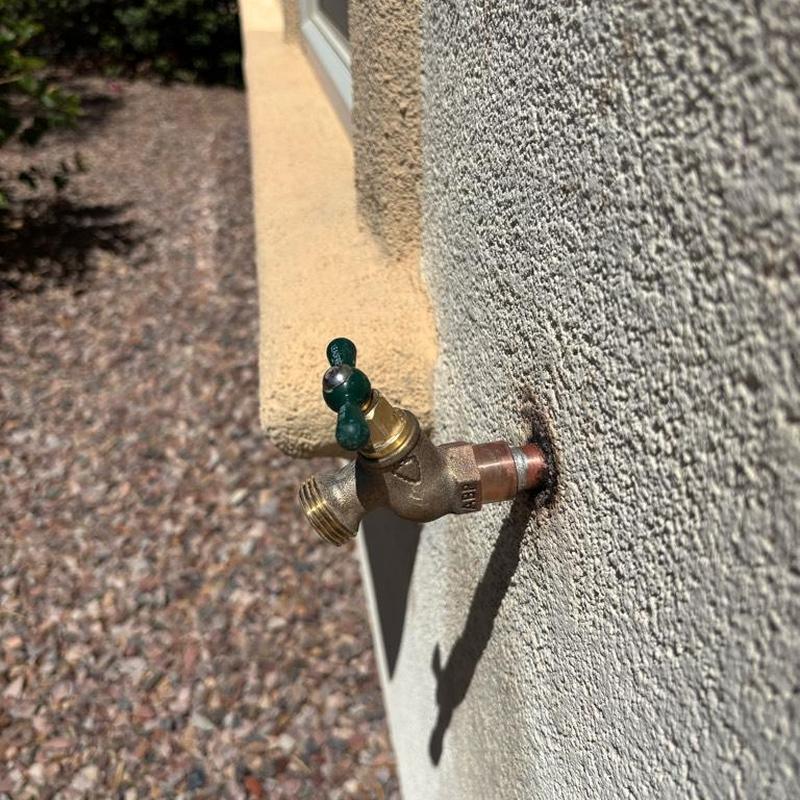 Hose bib valve with green handle on exterior wall