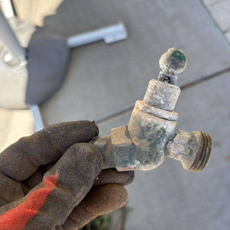 Outdoor hose bib faucet with corrosion held in gloved hand