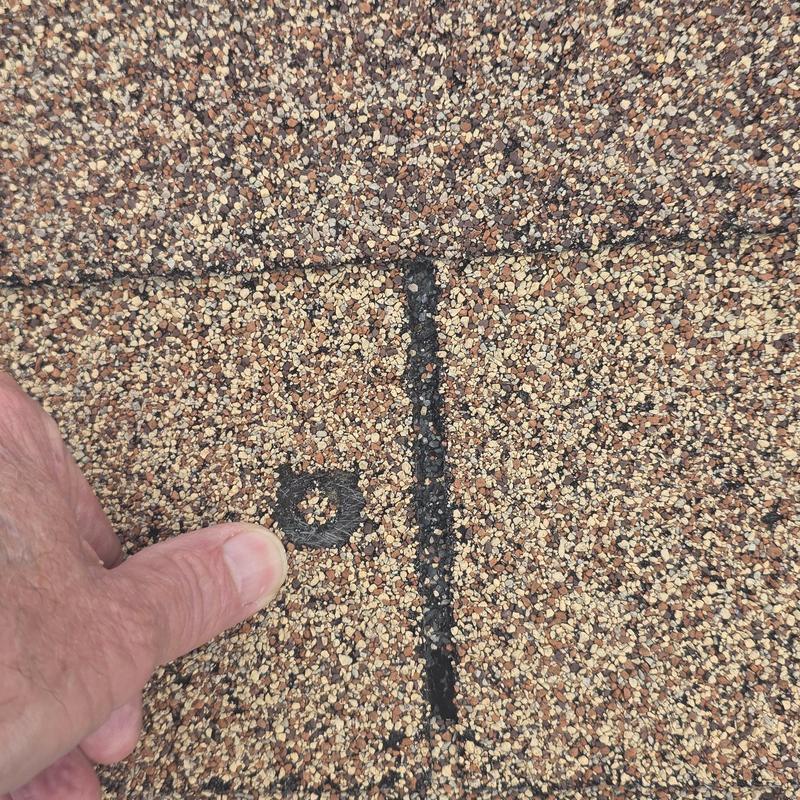 Asphalt roof shingle hail damage close-up with finger pointing