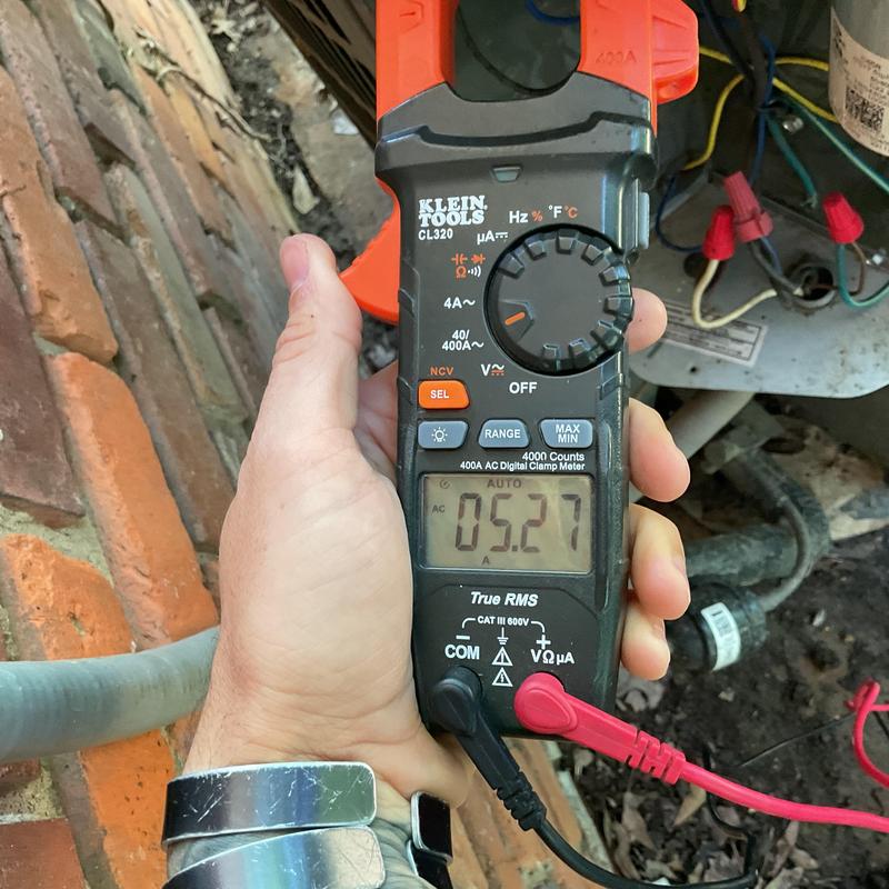 Clamp meter measuring HVAC electrical current at outdoor unit