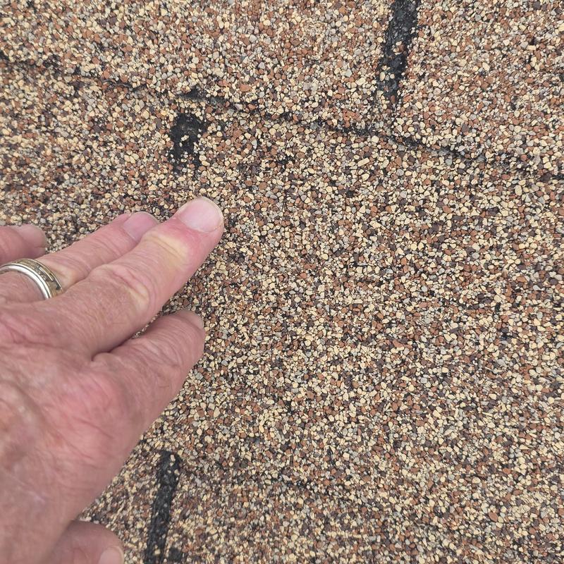 Asphalt roof shingle hail damage close-up with fingers