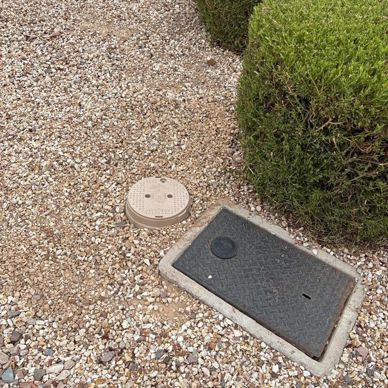 Water main valve access box and meter cover next to shrub