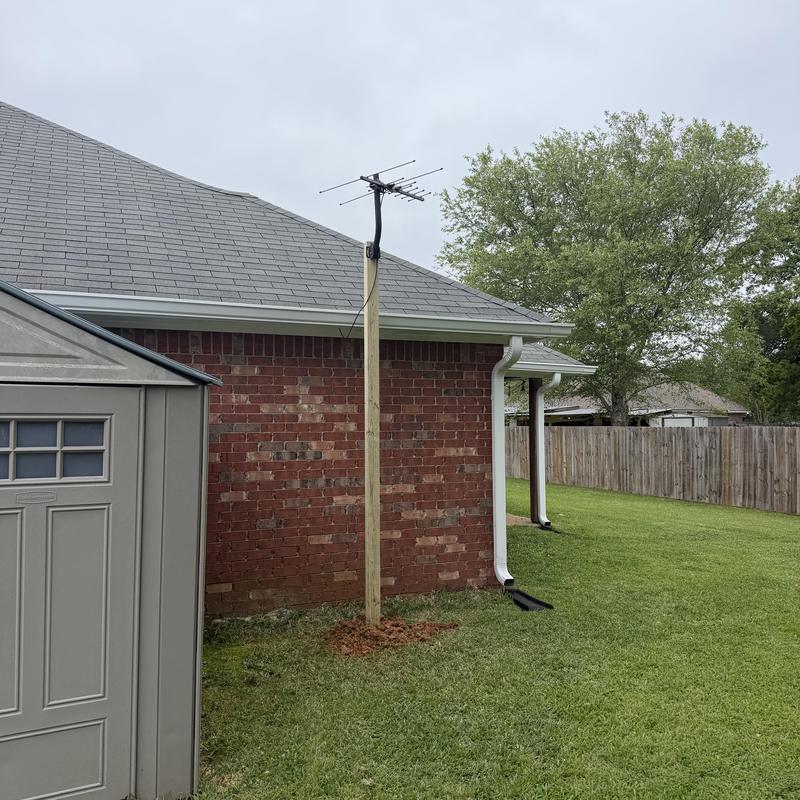Antenna mounted on 4x4 wooden post near brick house