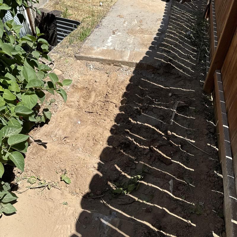 Sewer main trench backfilled near concrete walkway