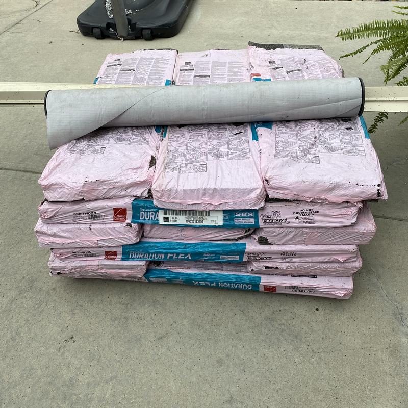 Asphalt shingle bundles and underlayment roll on ground