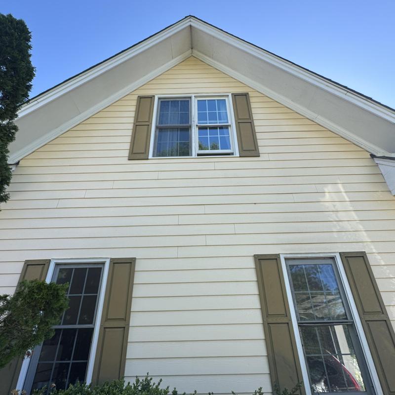 Upper window with brown shutters on beige siding Upper window with brown shutters on beige siding
