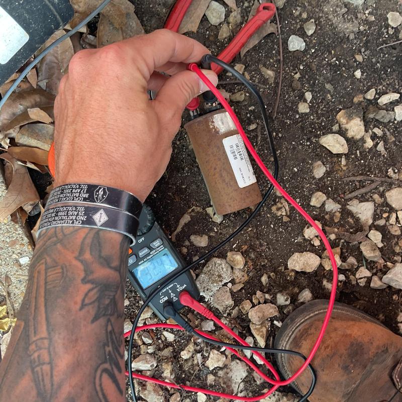 HVAC capacitor testing with multimeter on gravel ground