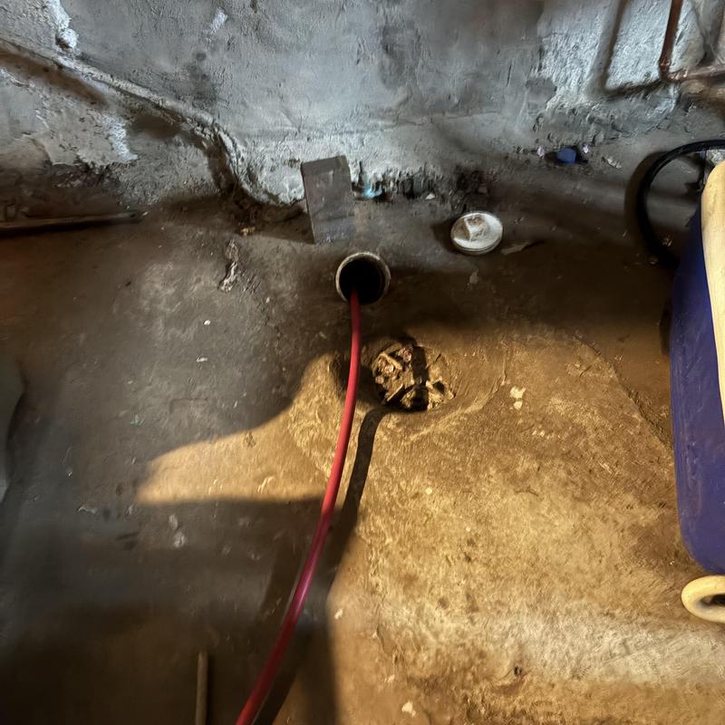 Drain pipe jetting with red hose in basement floor