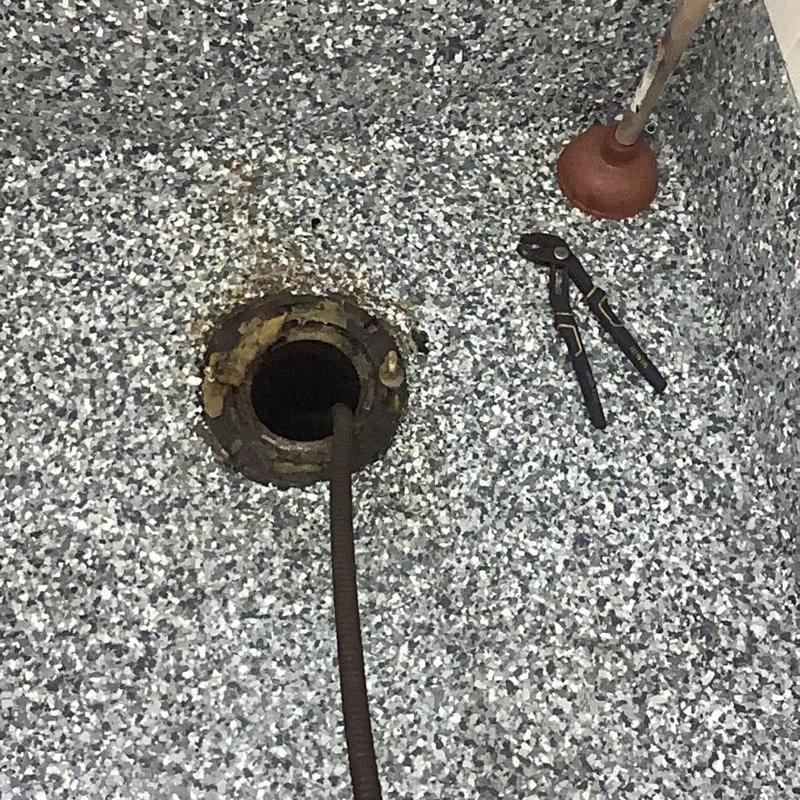 Toilet drain with plumbing snake and tools on floor