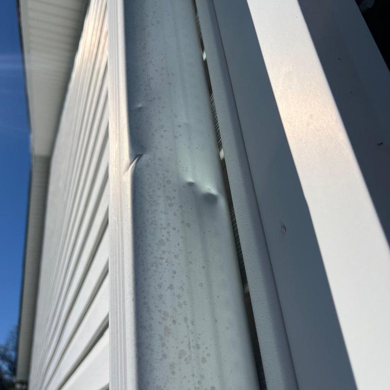 Metal gutter dented from hail damage on white siding wall