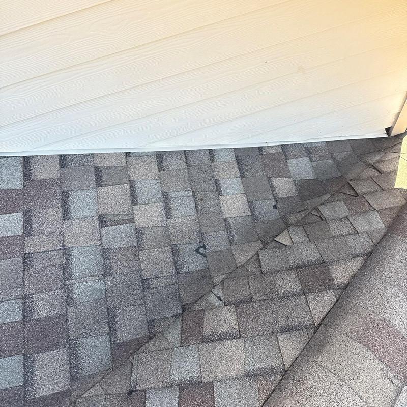 Asphalt roof shingles lifted for inspection near siding panel