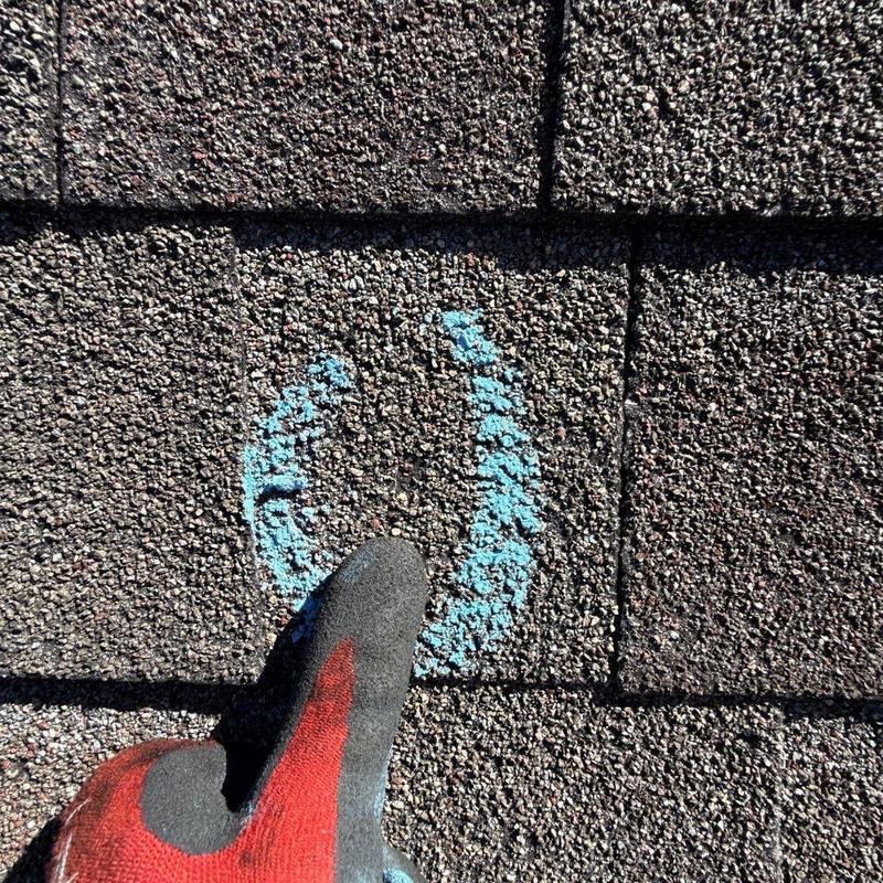 Hail-damaged roof shingle with marking and gloved finger
