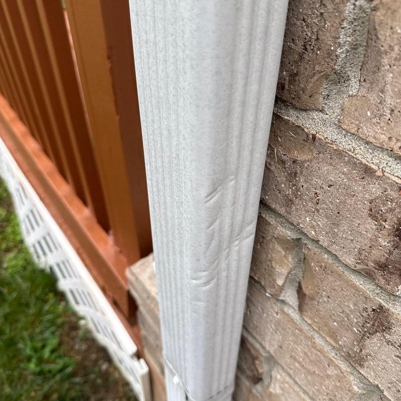 Downspout dent damage near brick wall and fence