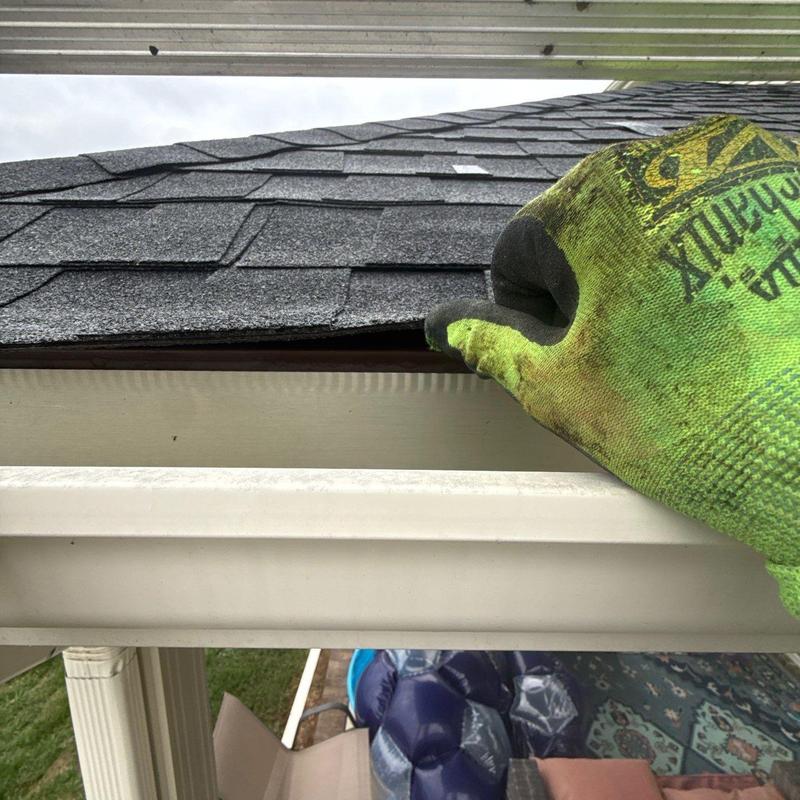Roof shingles inspection with gloved hand near gutter