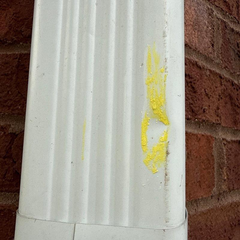 Downspout with yellow paint marks on brick wall background