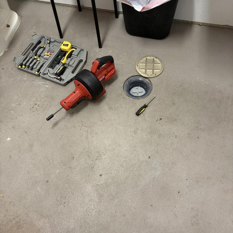 Floor drain with plumbing snake and tool kit on concrete floor
